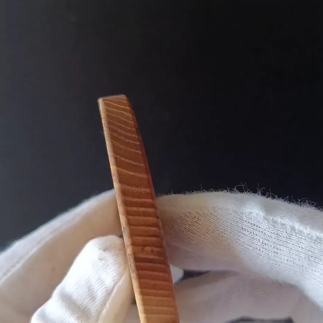 Ash wood coaster held on its edge in white cotton gloves, showing its thickness and the grain