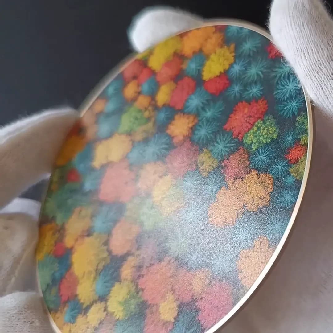 Autumn Forest coaster held at an angle in white cotton gloves, showing the printed front and the gold rim
