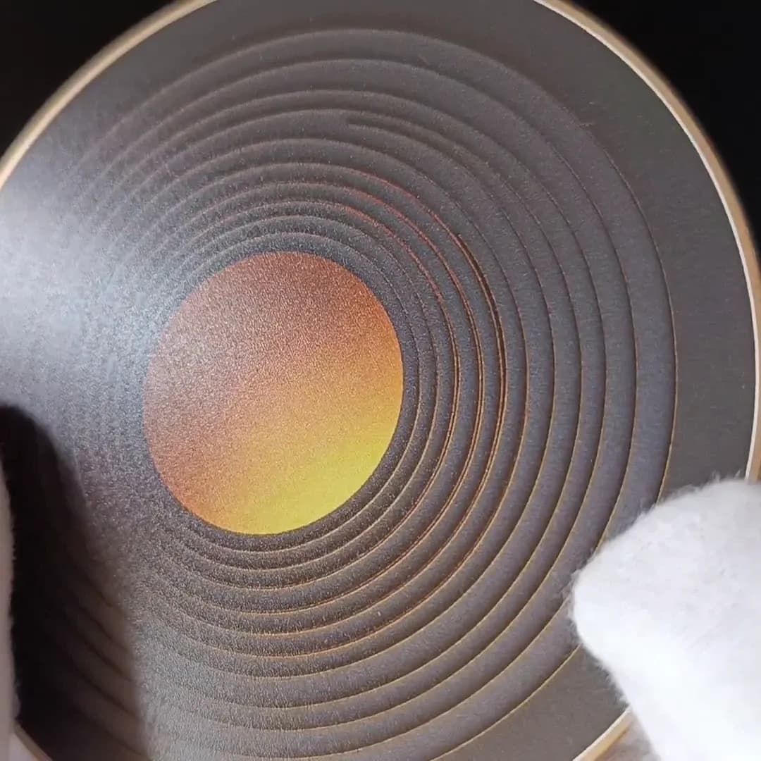 Gold Rings coaster held at an angle in white cotton gloves, showing the rings and the gold rim